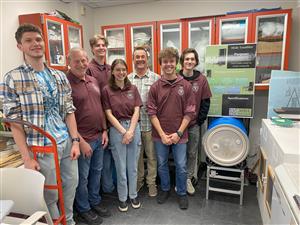 students stand with an invention designed to tumble hides at the academy of natural sciences